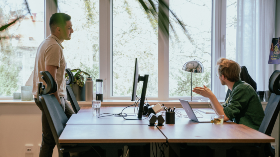 2 people sitting at each their side of a desk talking about a subject (Casual talking between colleagues)